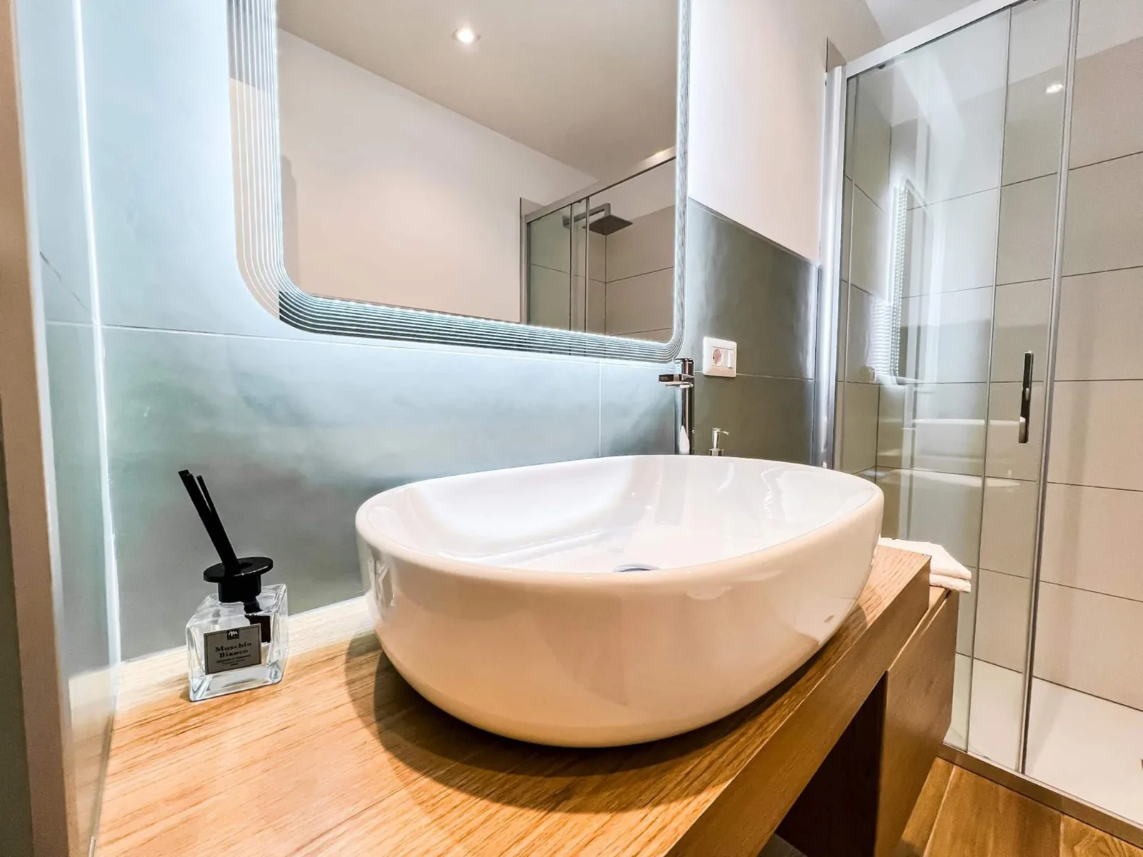 Il bagno visto dalla porta: lavabo, specchio a parete e box doccia a vetri