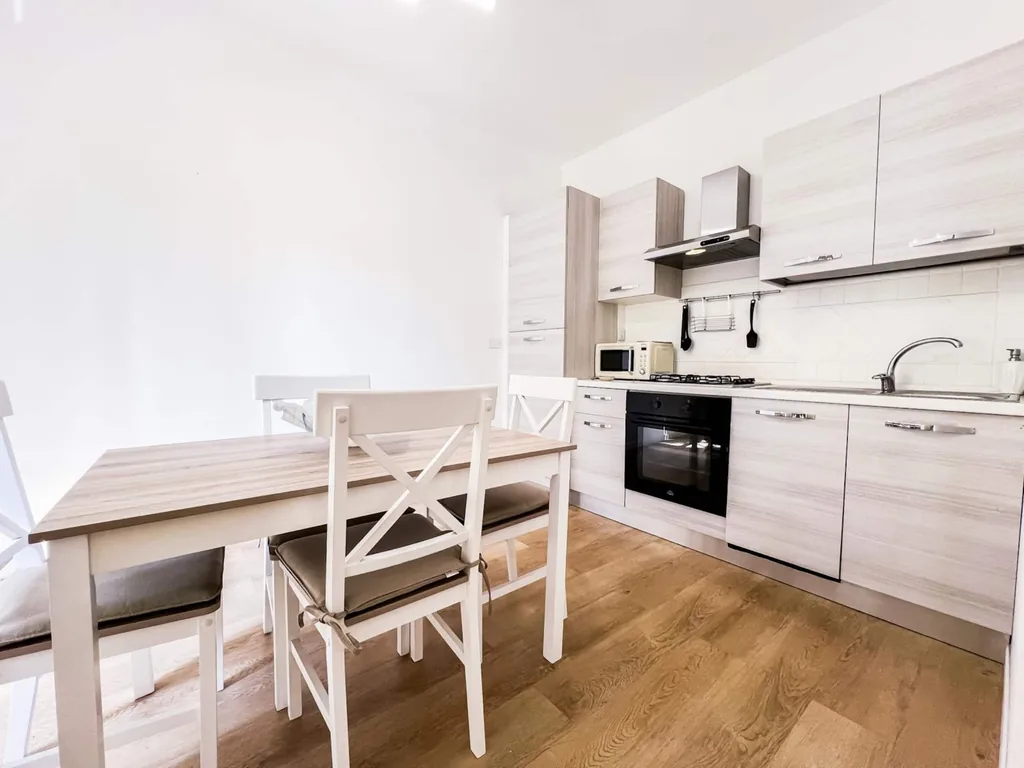 La cucina completa con tavolo, sedie bianche, forno, cappa e microonde