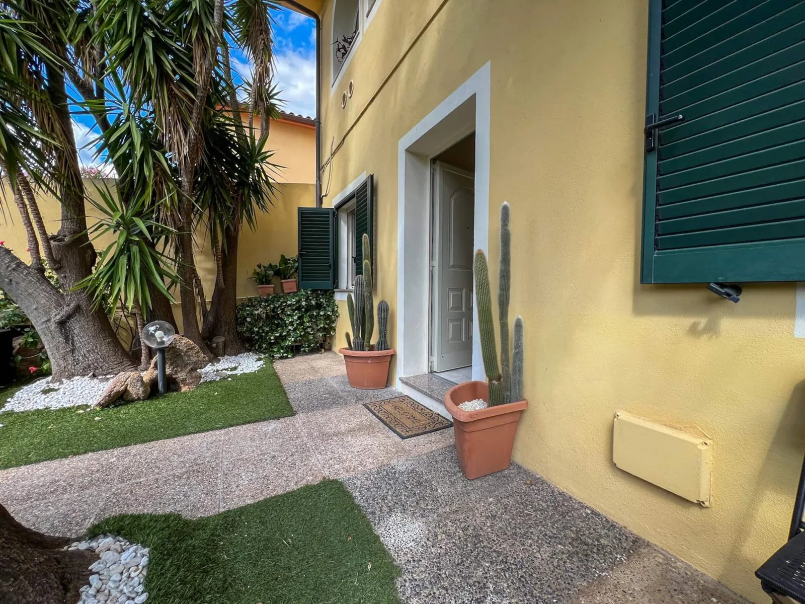 L'ingresso indipendente sulla facciata gialla, con prato, vasi di cactus e zerbino
