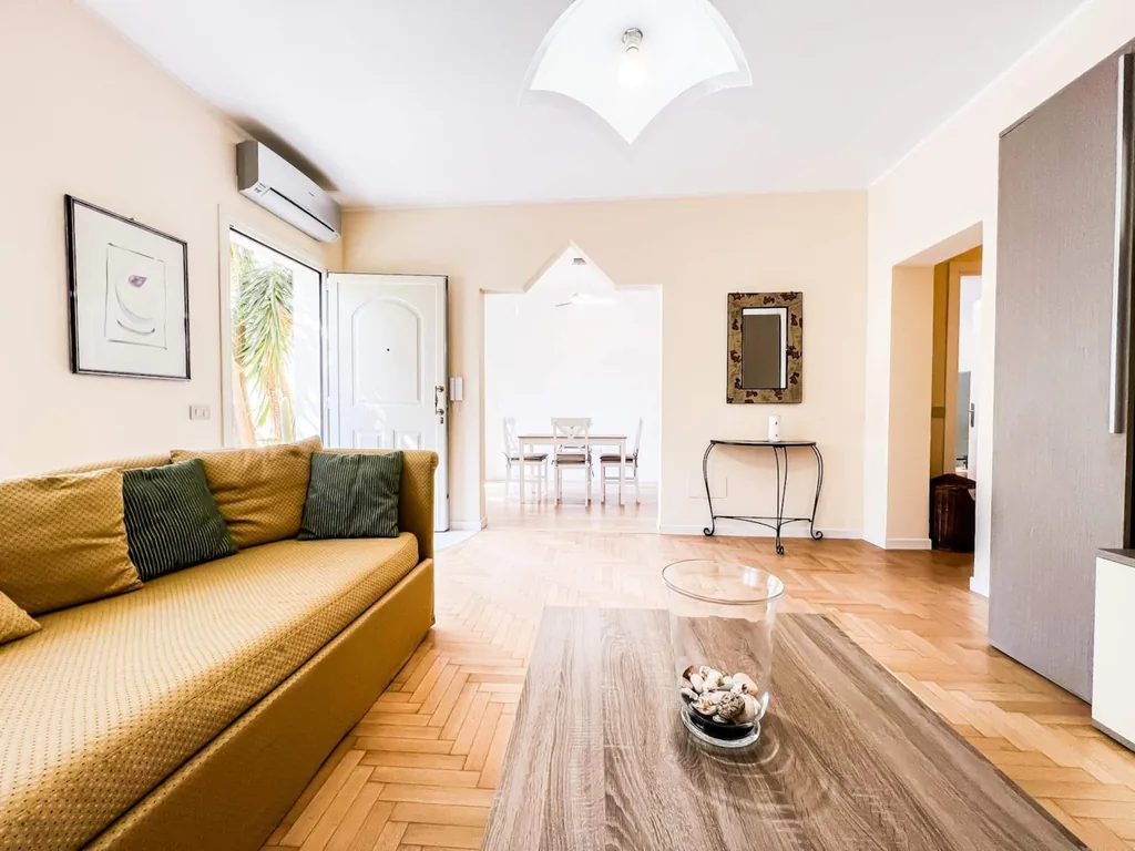 Il divano color senape del soggiorno, con la zona pranzo e la porta sul fondo