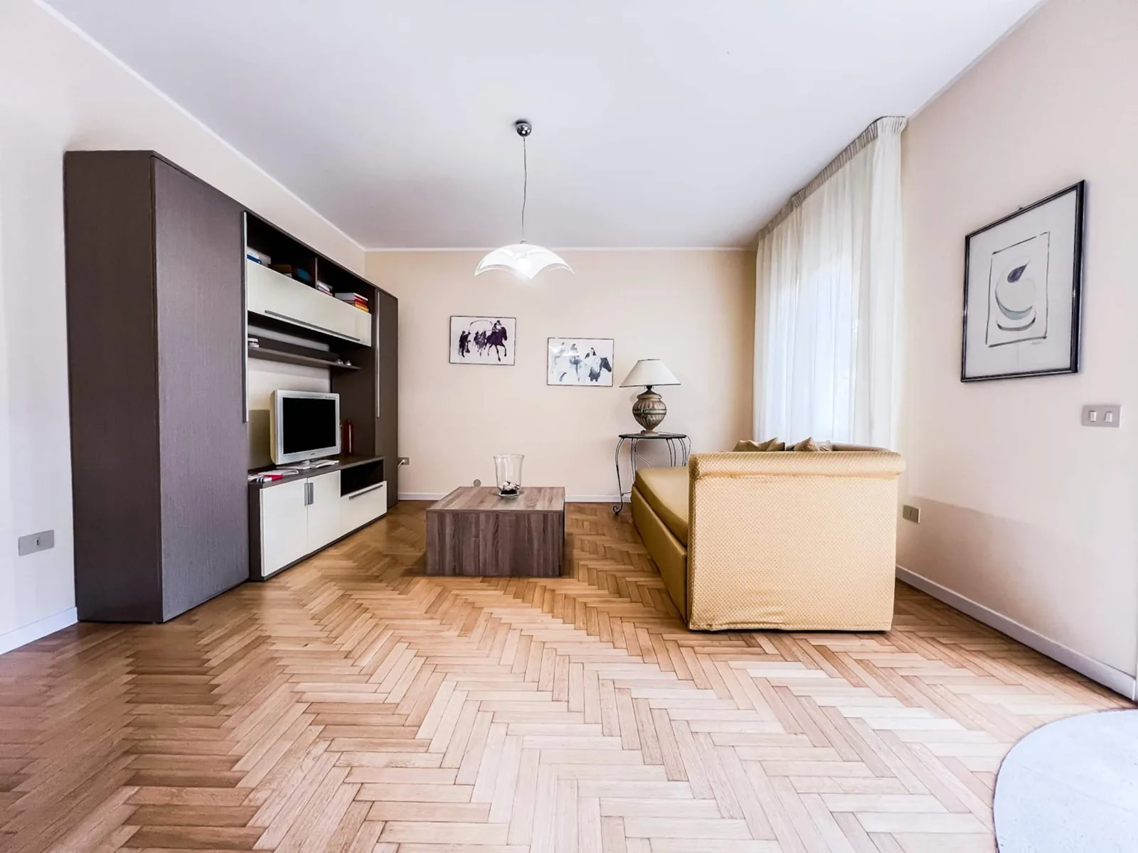 Il soggiorno dalla zona pranzo: mobile scuro con televisore, divano e finestra con tenda