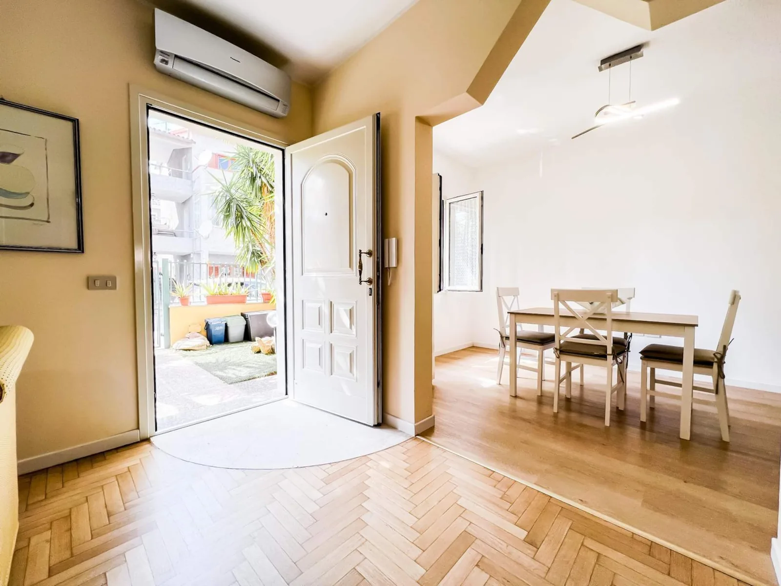 Soggiorno con tavolo da pranzo e porta d'ingresso aperta sul giardino, parquet a spina