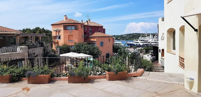 Scorcio della piazzetta di Porto Cervo con case rosa, vasi di terracotta e yacht sullo sfondo