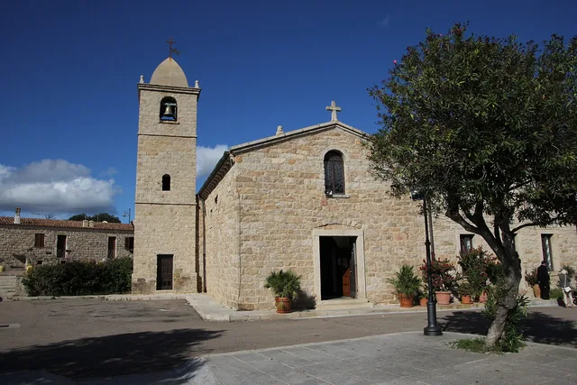 La chiesa in granito di San Pantaleo con campanile e oleandri in vaso sulla piazza