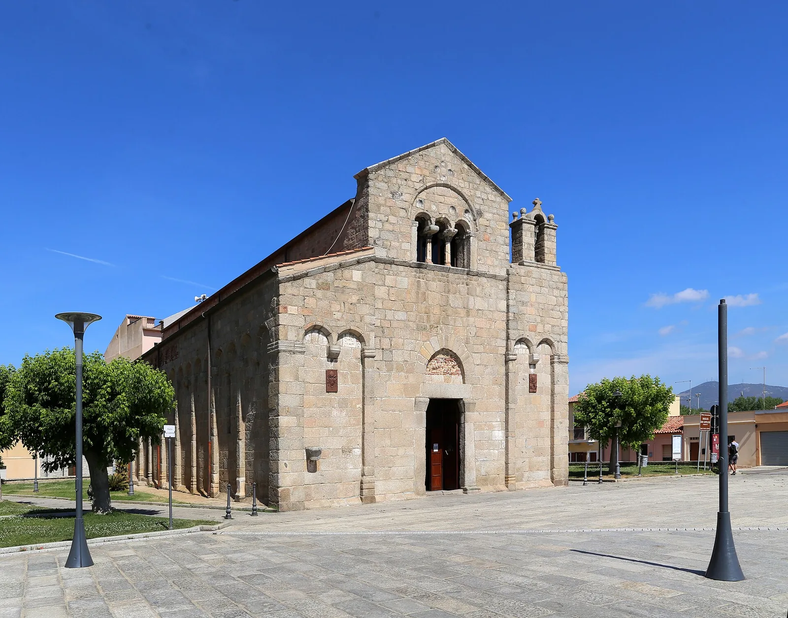 La basilica romanica di San Simplicio in granito, vista di sbieco dalla piazza assolata