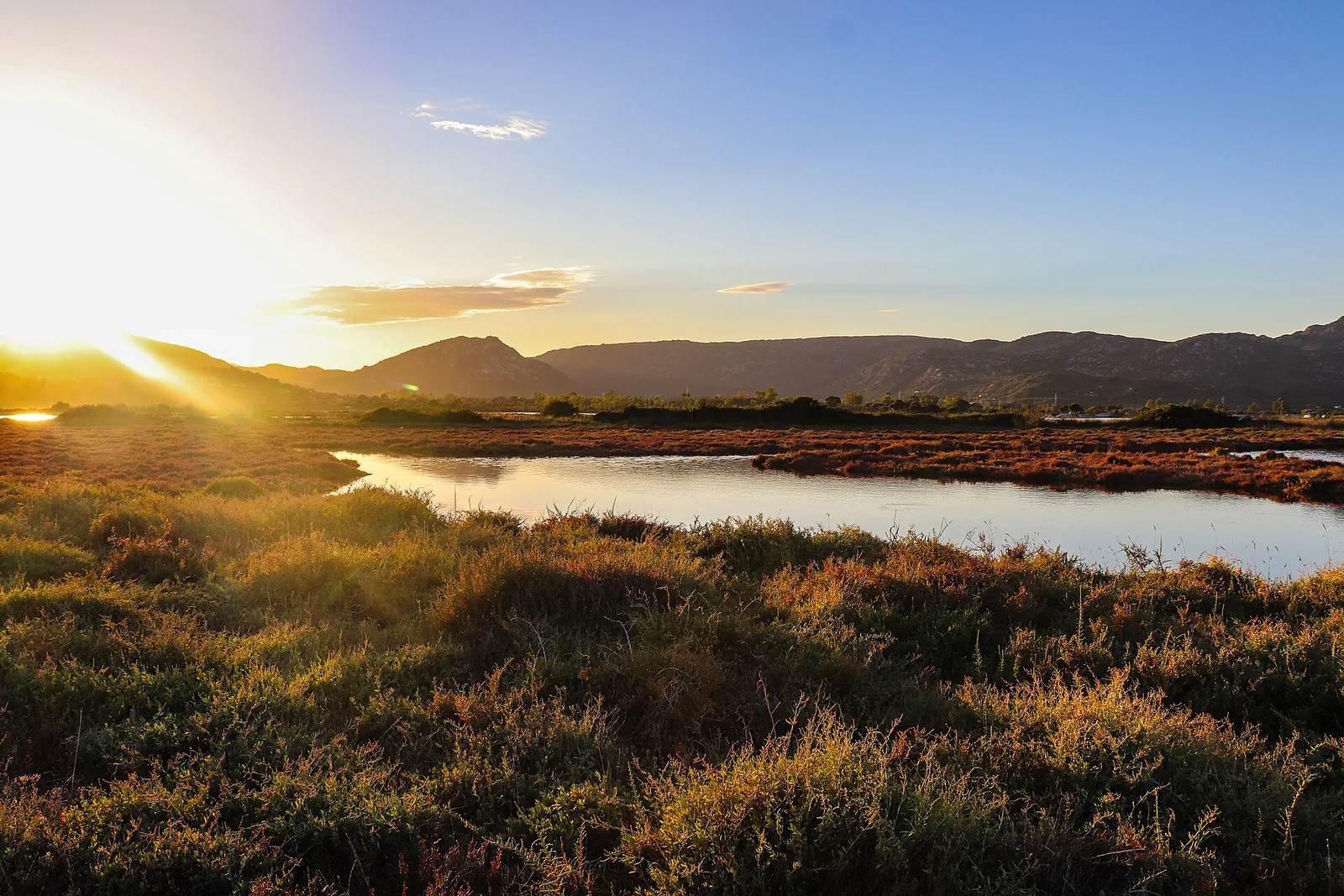 Luce calda del tramonto sullo stagno di San Teodoro tra canneti bassi e colline