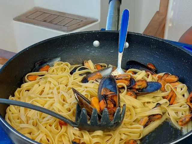 Padella di tagliatelle con le cozze servita in barca, mare turchese dietro