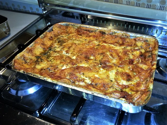Zuppa gallurese appena sfornata nella teglia, superficie dorata e gratinata con erbe, sul piano cottura